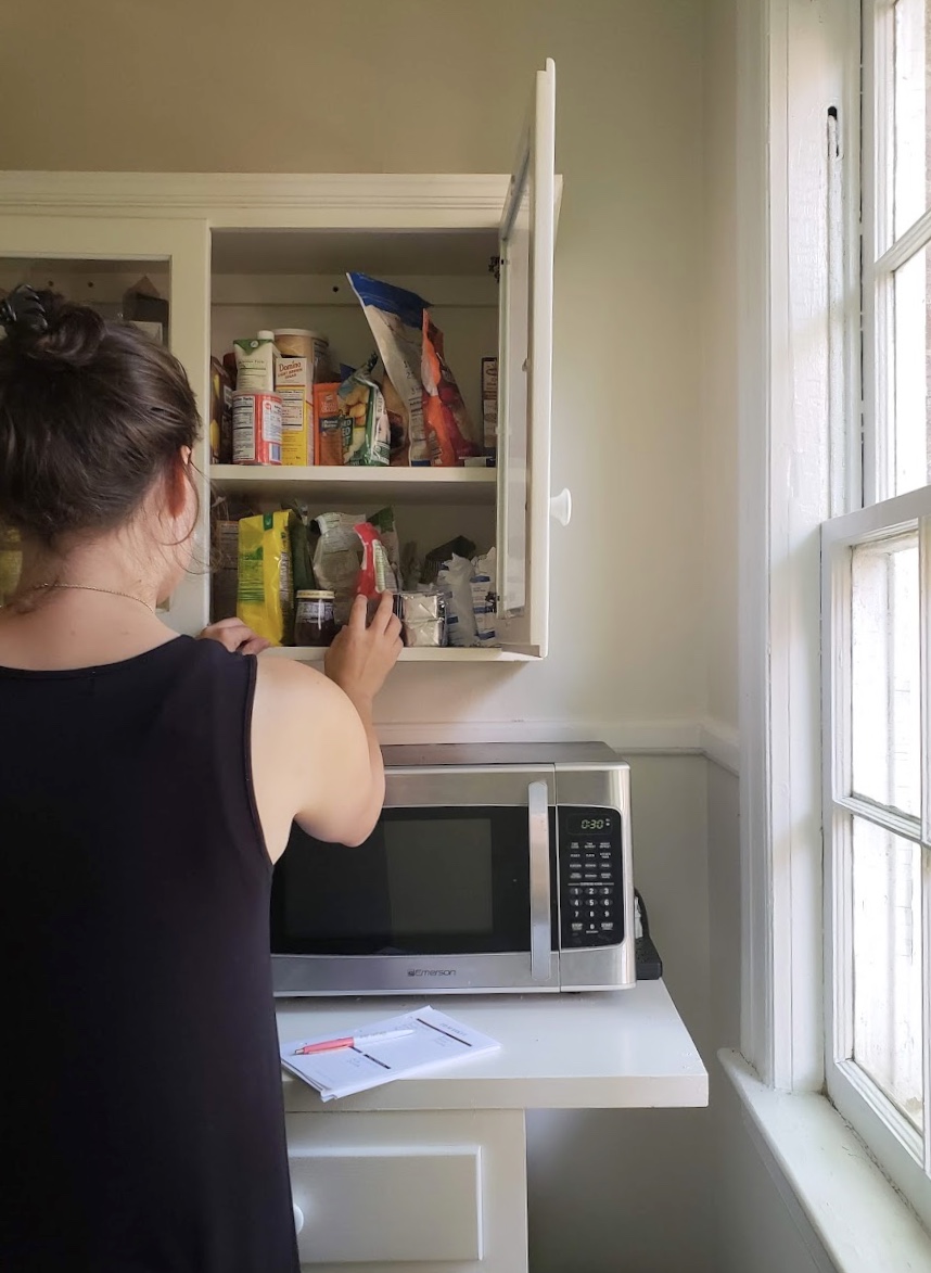 Woman reaches away towards a cupboard full of food packages.