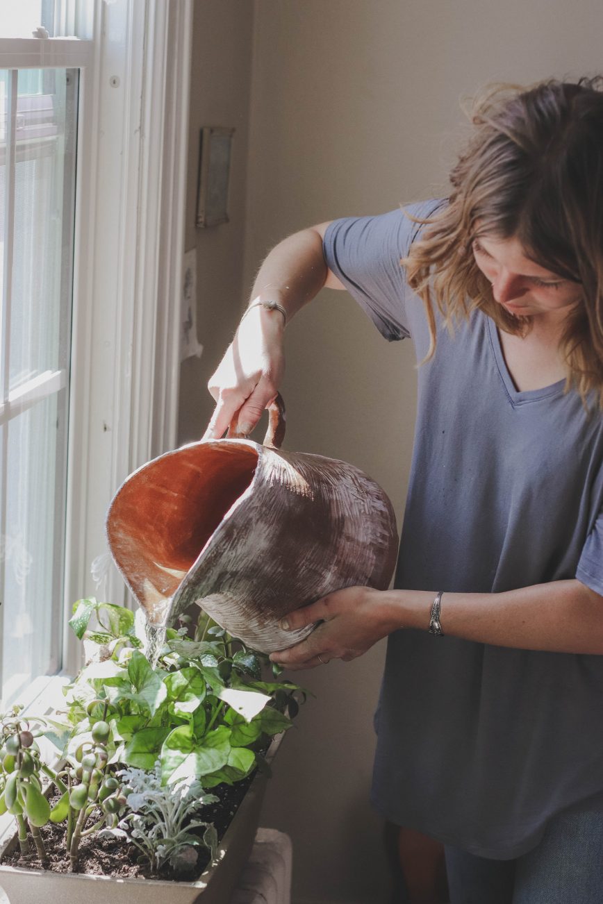 Woman watering plant beside window